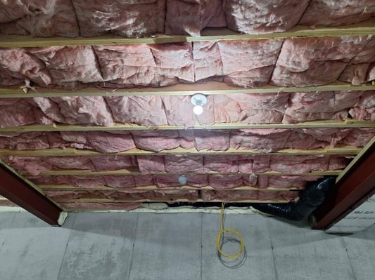 A basement ceiling insulated with fiberglass batts, paired with an air-seal in the basement rim joists.