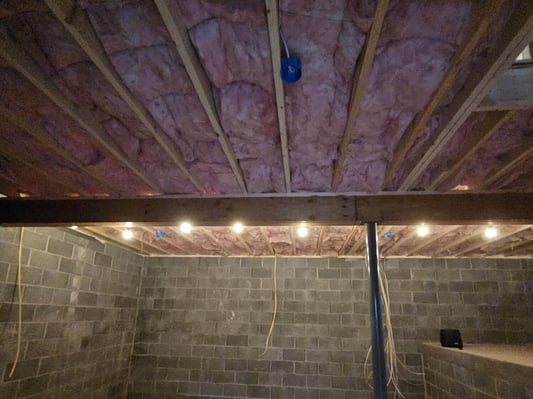 A basement with fiberglass batt insulation in the ceiling.