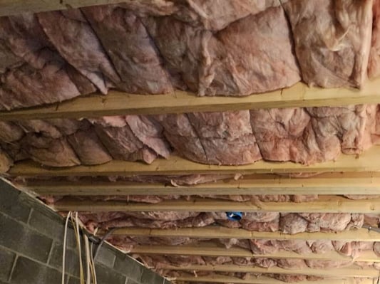 A basement ceiling insulated with fiberglass batts.