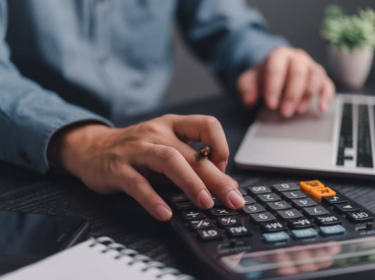 A man using a calculator and laptop to estimate the cost of his dream home.