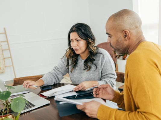 A couple researching homes online on their computer and with printouts.