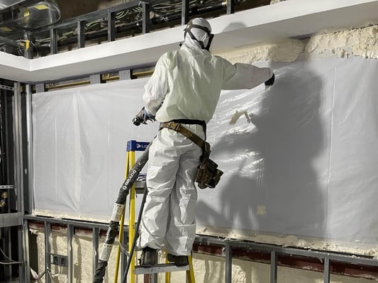 A spray foam insulation contractor standing on a ladder while installing closed cell foam.