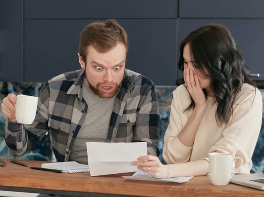A man and woman looking at their energy bill. The man is shocked by the high cost.