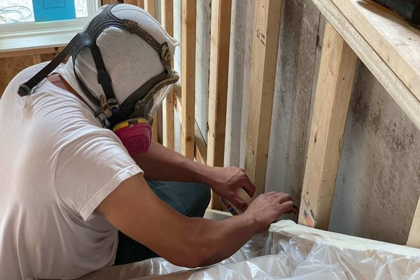 A spray foam insulation crew member prepping a new construction home for spray foam. He is wearing a respirator and head sock.