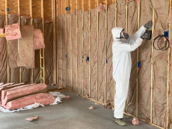 An insulation contractor fastening fiberglass batt insulation to wood wall cavities with staples.