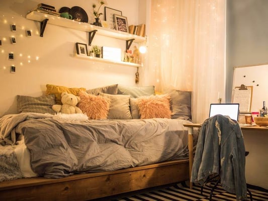 An image of a kid's bedroom with fairy lights, a jean jacket, a teddy bear, and lots of throw pillows.