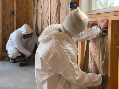 Insulation contractors installing fiberglass batts in a garage while wearing an N95 mask for personal protective equipment (PPE).