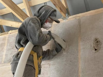 An insulator contractor installing dense pack cellulose into a garage while wearing an N95 mask.