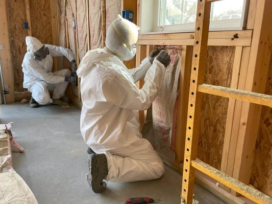 Insulation contractors in Greencastle, PA, installing fiberglass batt insulation. The contractors wear PPE to protect their eyes and skin.