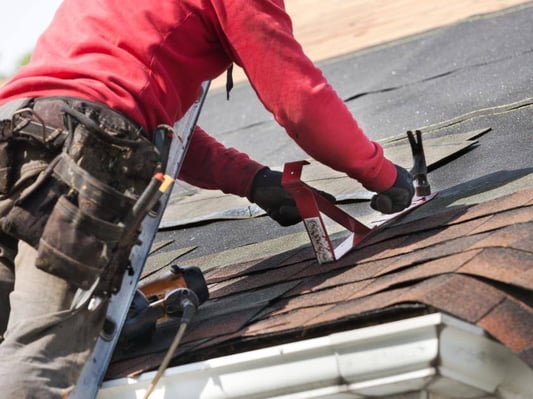 A roofer working with shingles on the top of a roof.