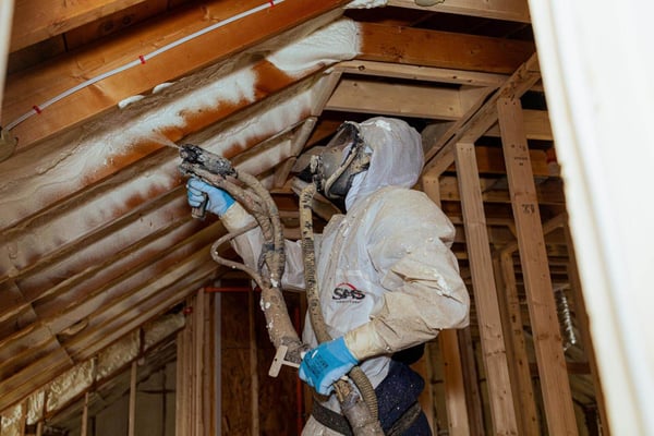 A spray foam installer at South Central Services installing closed cell spray foam in Chambersburg, PA while wearing a moon suit.