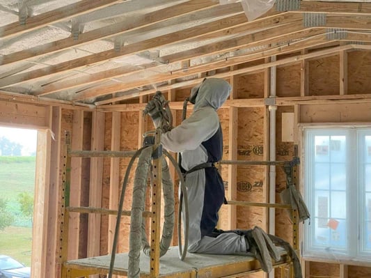 A spray foam technician working in a new construction home in Fayetteville, Pennsylvania. He is installed closed cell spray foam in the roof overhead.