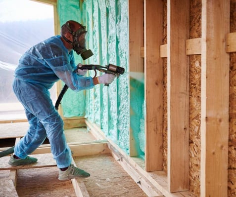 A spray foam installer insulating with dyed blue spray foam insulation in a new construction wall cavity.