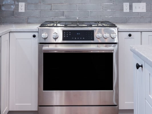 A stainless steel oven in a kitchen with stone countertops and white cabinets.