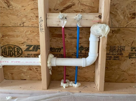 Pipes and water hook-ups in a new construction home prepped for spray foam. Potential air leaks are sealed with can foam.