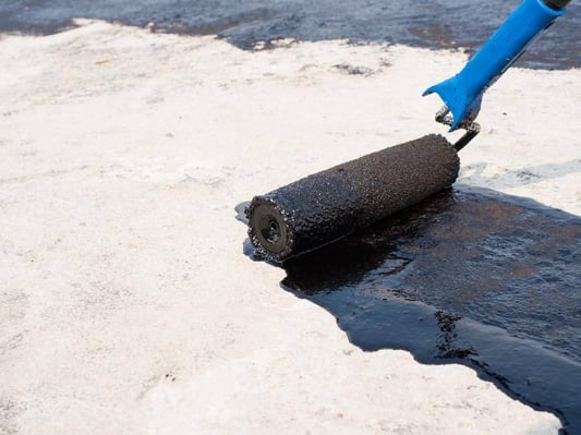 A roller with a waterproof coating being applied to a concrete surface.