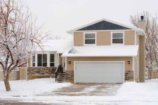 A home with a second story over its garage after a snow fall. The driveway is shoveled, but the yard, roof, and tree have snow clinging to them.