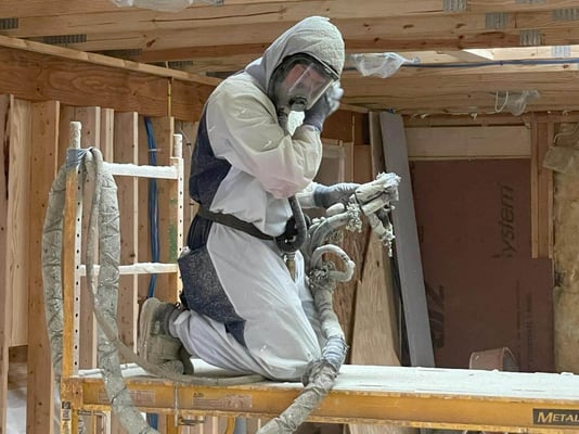 A spray foam insulation installer wiping the face shield of his fresh air system after spraying overhead.