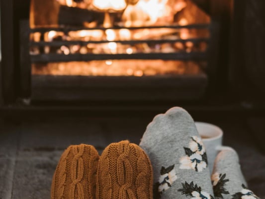 Two people wearing cozy socks in front of a roaring fire in a fireplace indoors.