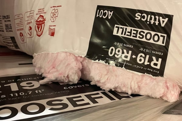 Bags of loose fill fiberglass insulation. The product R-value ranges from R19 to R60. One bag of insulation is open with the fiberglass visible.