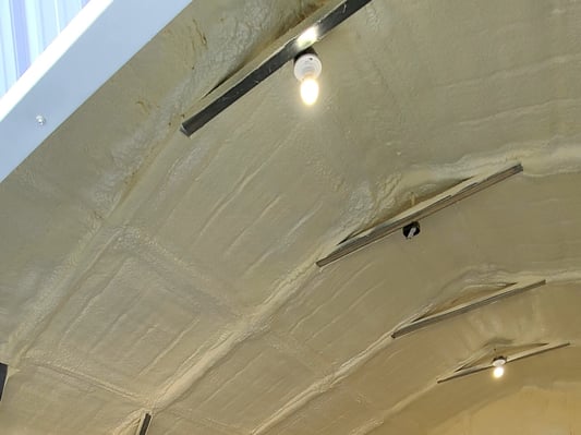 A close-up of the ceiling of a metal building, insulated with closed cell spray foam insulation.