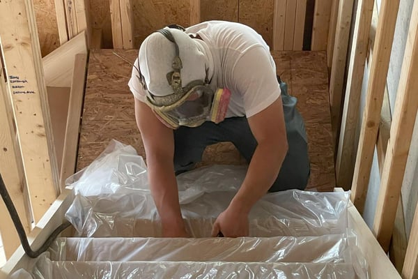 A spray foam insulation contractor prepping a new construction home for spray foam insulation, covering stairs with plastic sheathing.