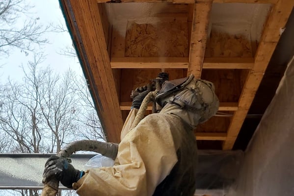 A spray foam insulation contractor spraying foam overhead into a wooden cavity.