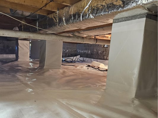 A crawl space with pillars, wrapped in plastic sheathing to act as a vapor barrier. The seams are sealed with professional crawl space tape.