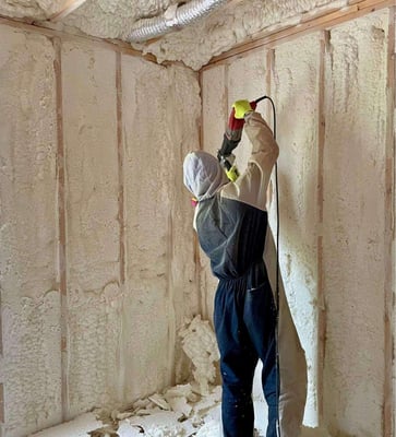A spray foam insulation crew member shaving excess open cell spray foam from wall cavities.