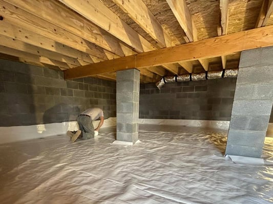 A contractor in southern PA encapsulating a crawl space. He is sealing the edges of the floor's vapor barrier with crawl space tape.