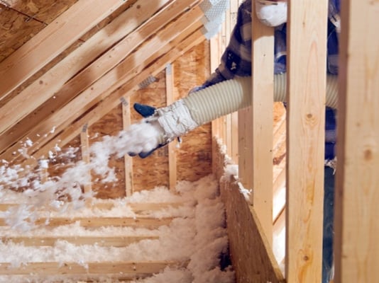 A contractor installing blown-in fiberglass insulation into an attic.