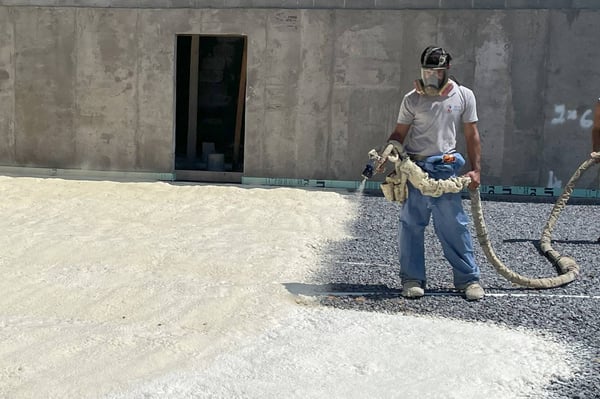 A professional spray foam contractor installing closed cell spray foam on a flat surface outdoors.