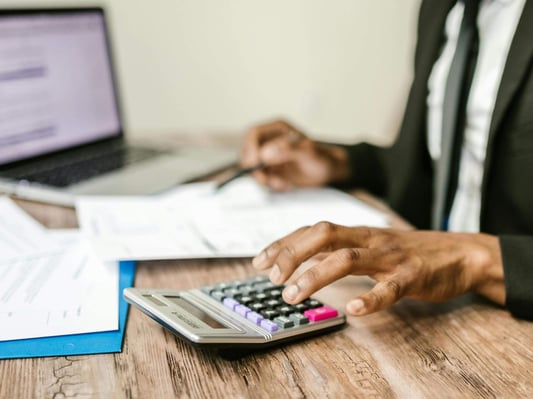 A person calculating their taxes with a physical calculator and laptop.