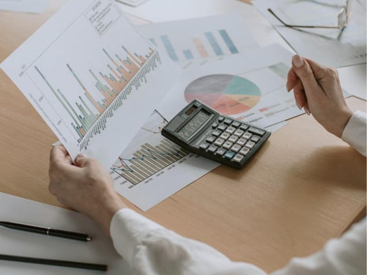 Someone examining charts and graphs at a table. They are using a calculator to estimate the cost of an investment.