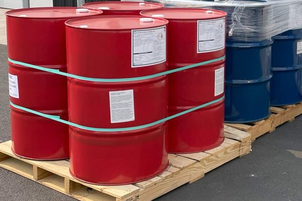 55 gallon drums of spray foam insulation components. The drums are red and blue, sitting on a wooden pallet.