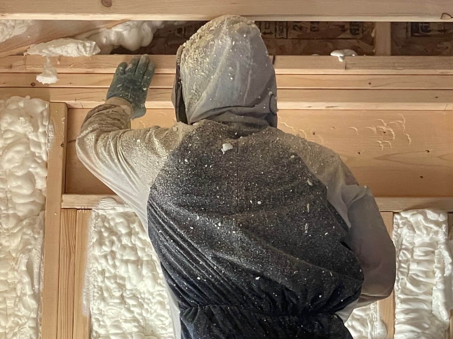 A spray foam insulation installer wearing personal protective equipment while spraying open cell foam.