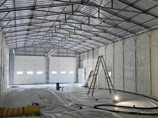 A pole building with garage doors being insulated with closed cell spray foam insulation.