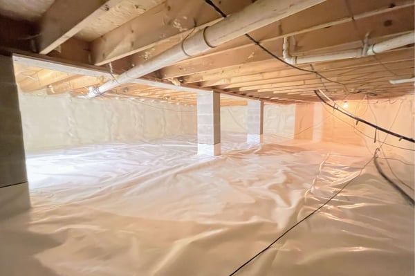 An encapsulated crawl space with pillars, ductwork, and wiring. The walls are insulated with closed cell spray foam and the floor has a vapor barrier.