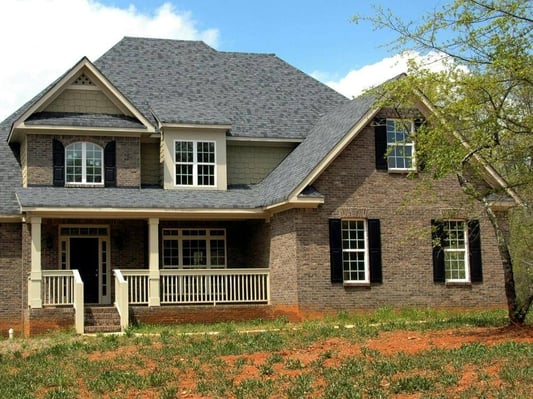 A two-story home with a front porch and a tree in the front yard.