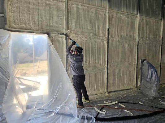 A team member at South Central Services scraping excess foam from a metal building for a clean finished look.