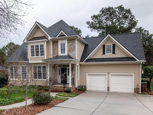 A house will yellow siding, two car garage, and an intricate roof.