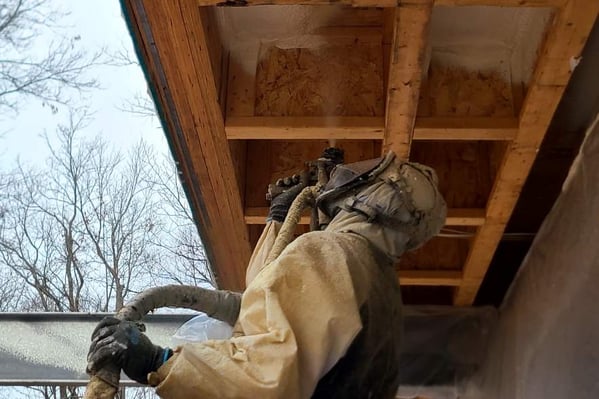A spray foam insulation contractor installing spray foam overhead into wood cavities.