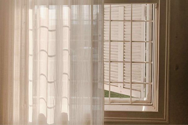 A window with a shutter, a sheer curtain, and sunlight streaming inside.