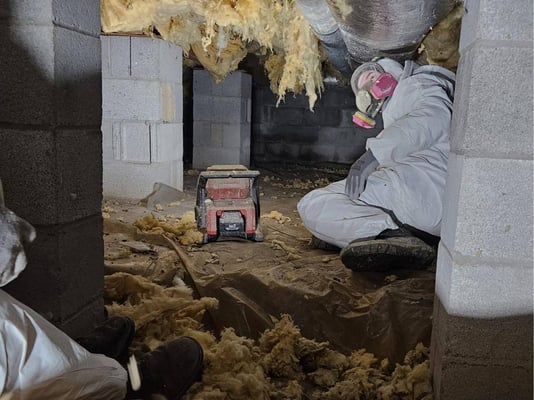 A spray foam installer in a crawl space with fiberglass batt insulation falling from the ceiling. The fiberglass absorbed moisture in the crawl space.