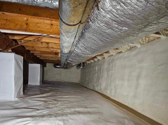 An encapsulated crawl space with wrapped pillars and HVAC vents. The spray foam in the rim joists is visible.