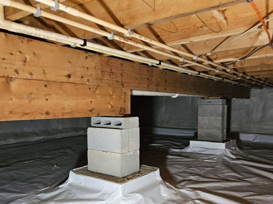 An encapsulated crawl space with pillars wrapped in plastic sheathing.