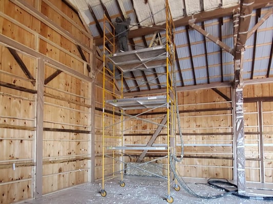 A spray foam insulation contractor on scaffolding to installing closed cell spray foam onto a metal bank barn roof.