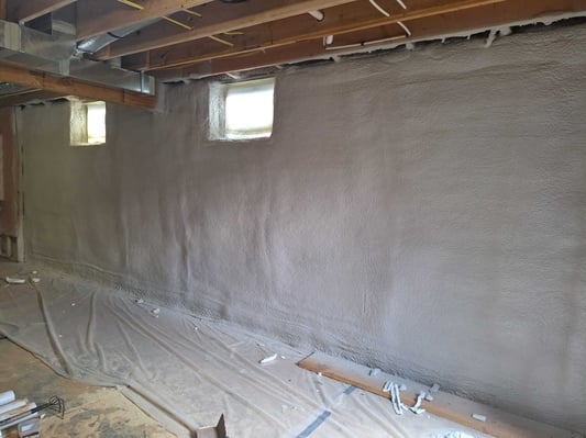 A basement insulated with closed cell spray foam. The floor and windows were protected from overspray with plastic sheathing.