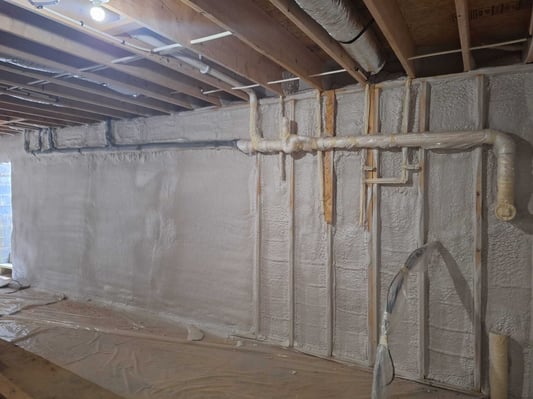 A basement wall with plumbing. The plumbing was protected with plastic to protect from overspray.