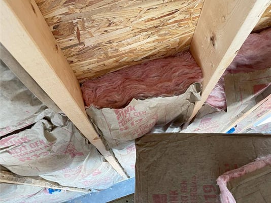 Fiberglass bat insulation installed in a wall. The fiberglass fits snugly and is touching all the surfaces of the cavity with no gaps.